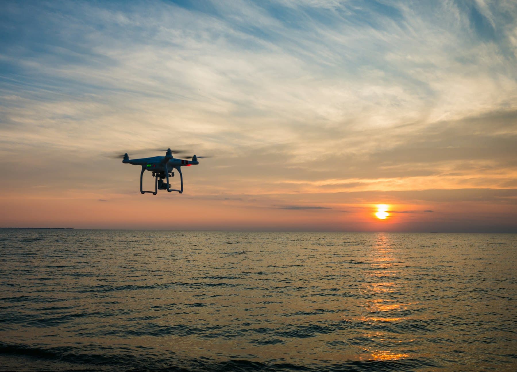 A small drone flies over open sea at sunset, far from land