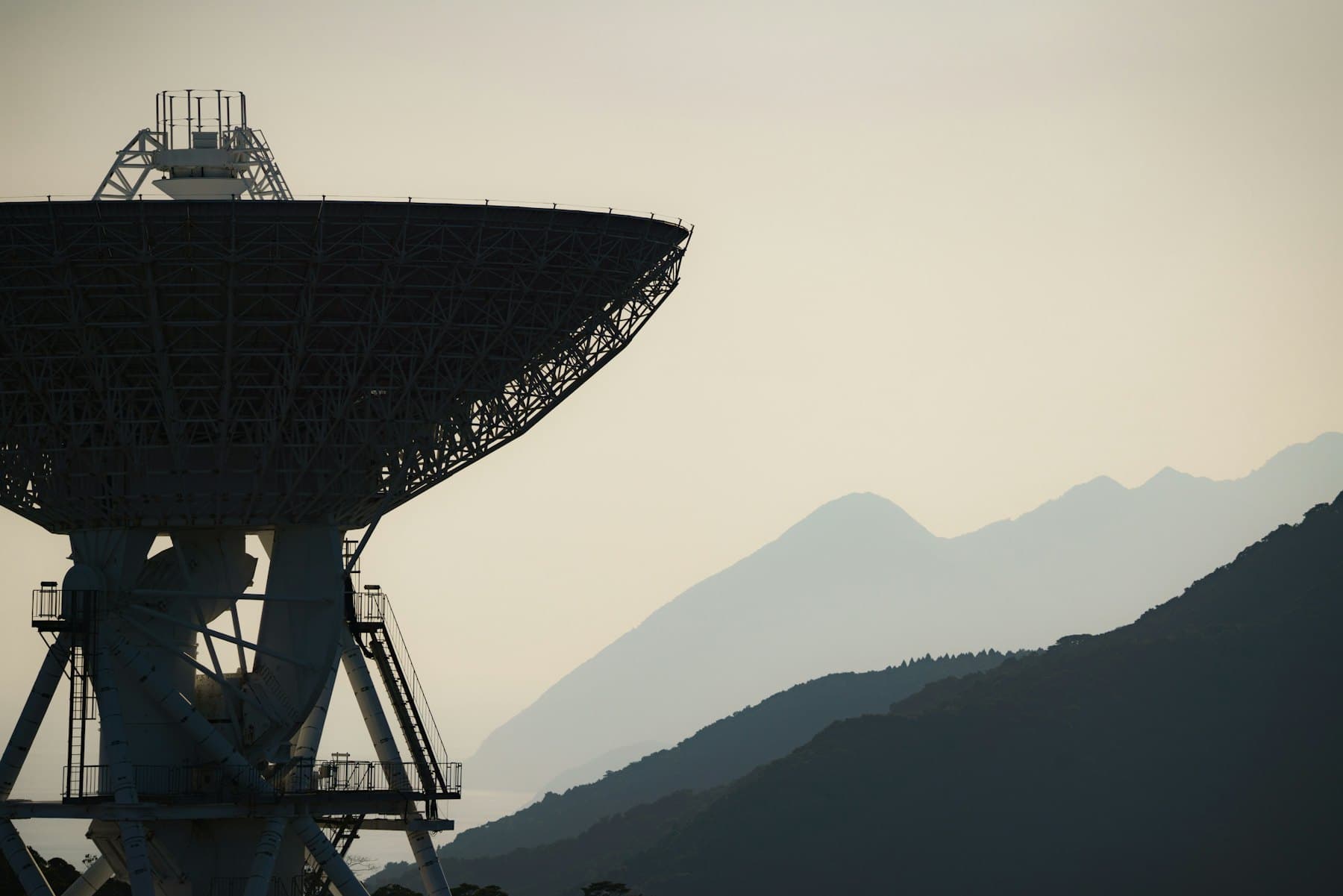 A large satellite ground-station dish against hazy mountains